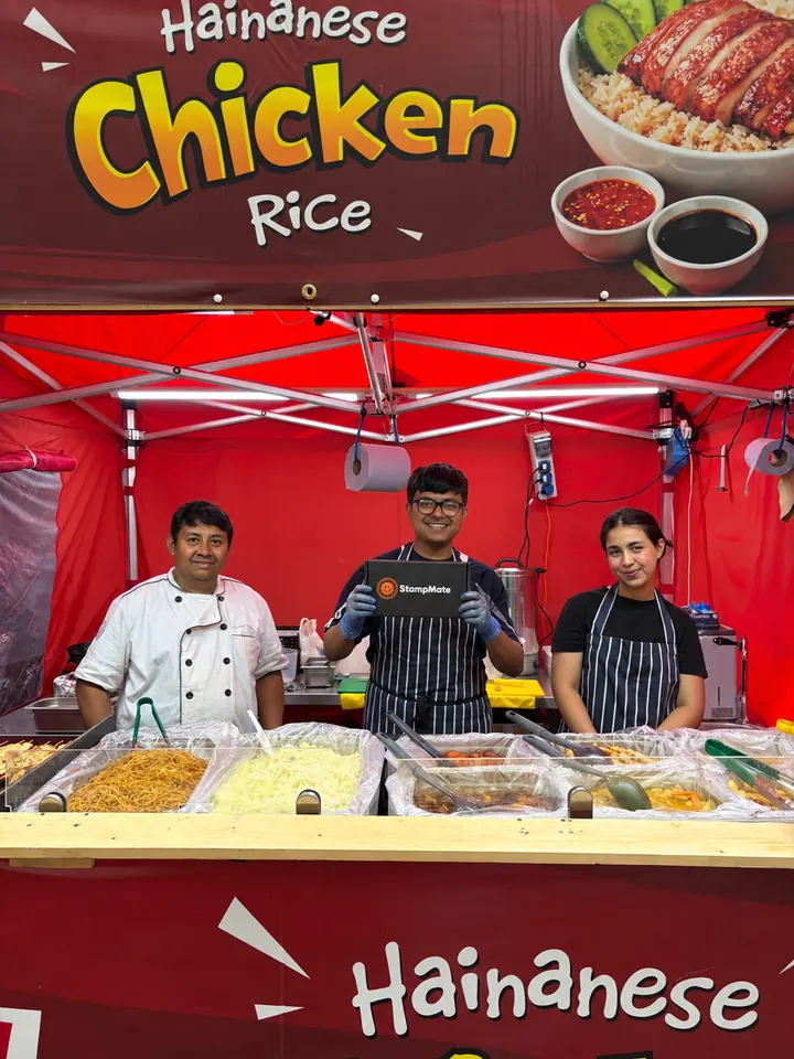 Three stallholders behind a Hainanese chicken rice counter holding a StampMate box