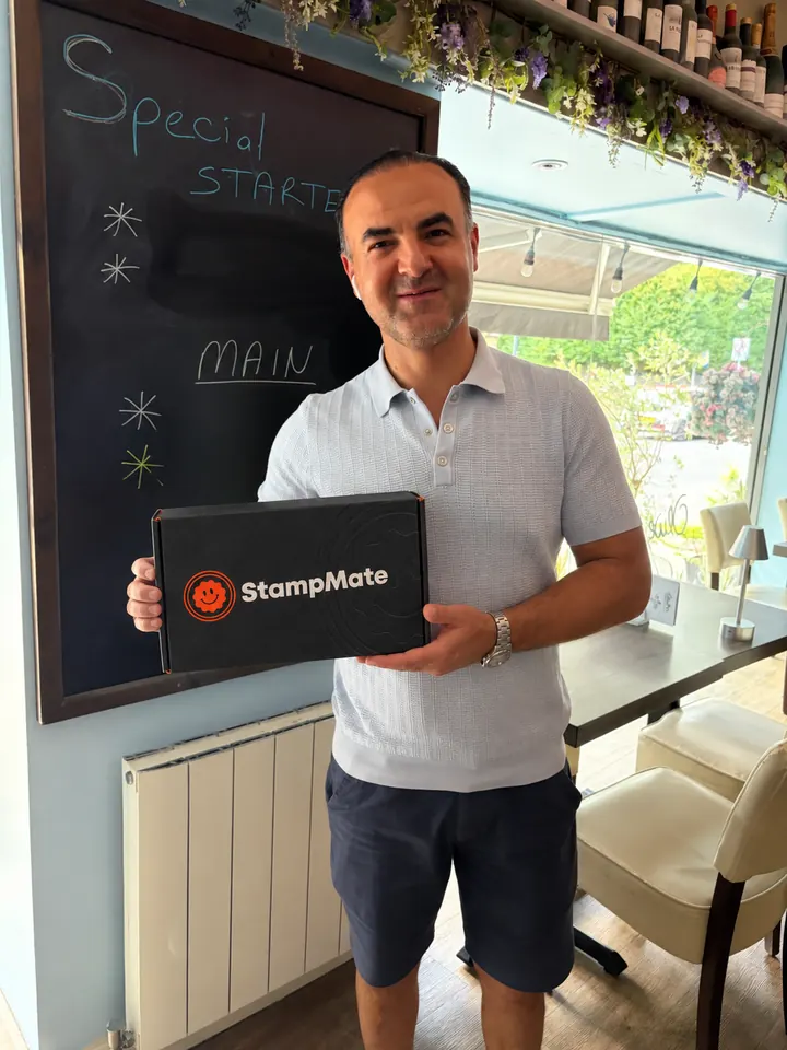 Man in a restaurant holding a StampMate box in front of a chalkboard menu