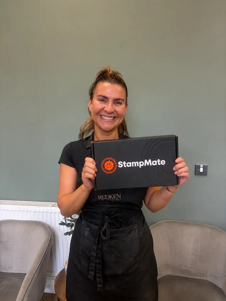 Hairdresser in a black apron holding a StampMate box in a salon