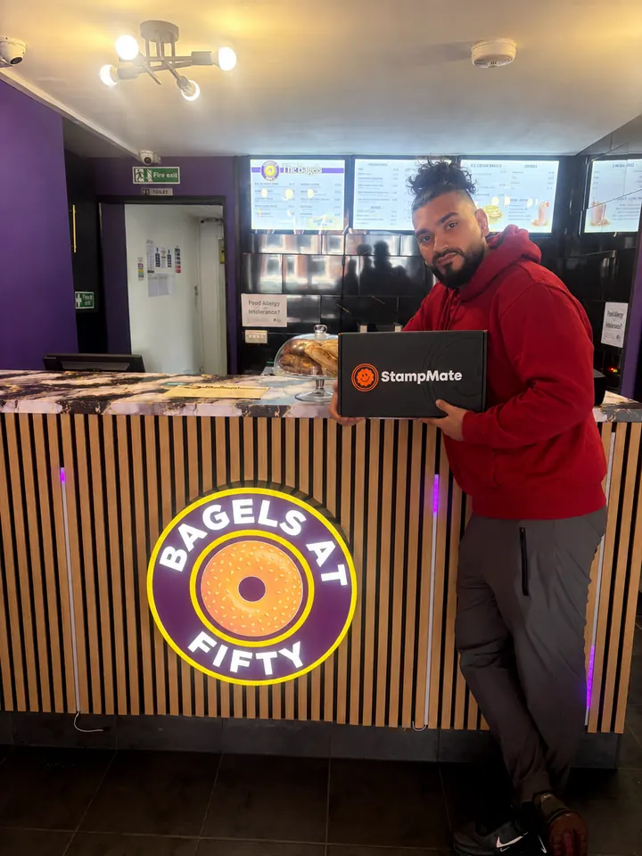 Man leaning on a bagel shop counter holding a StampMate box